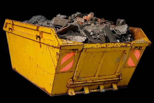 A large yellow industrial skip filled with a mixture of broken concrete, bricks, and rubble, situated outdoors on a paved surface. The skip has a sturdy metal construction with visible rust and scratches, and features reflective pink and grey safety markings on the sides. The material inside appears to be compacted and uneven, with fragments of varying shapes and sizes. The environment around the skip suggests an outdoor construction or renovation site, indicative of waste removal services typical in urban areas such as Oxford. The background is black, emphasizing the skip and its contents, which are photographed in natural daylight, highlighting the textures and colors of the debris. This image reflects the type of waste that Commercial Waste Oxford’s rubbish removal services might handle for clients in the Oxford area, focusing on construction and building waste disposal.